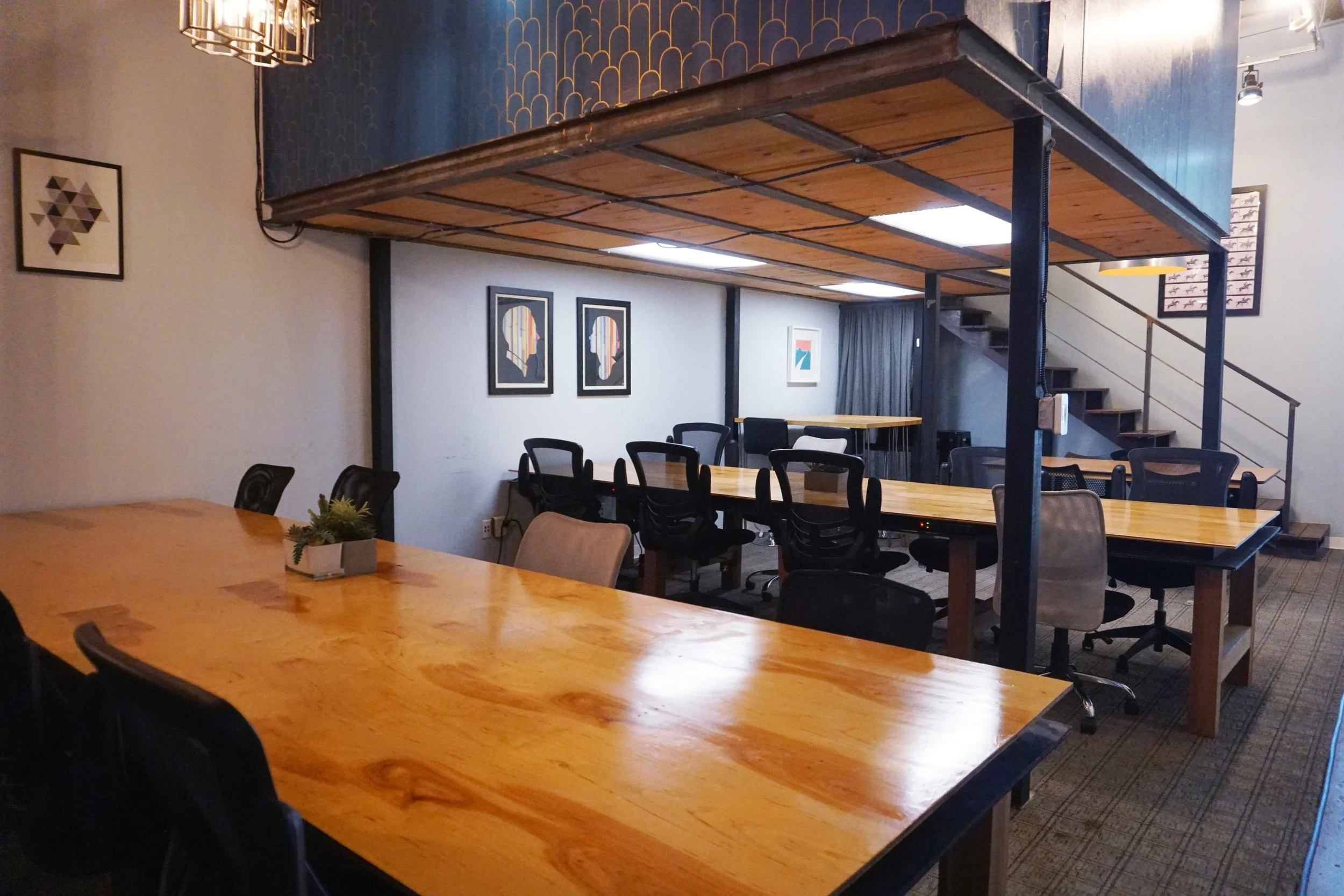 Createscape Coworking with warm wooden communal tables, mezzanine loft, art prints, and blue accent wallpaper