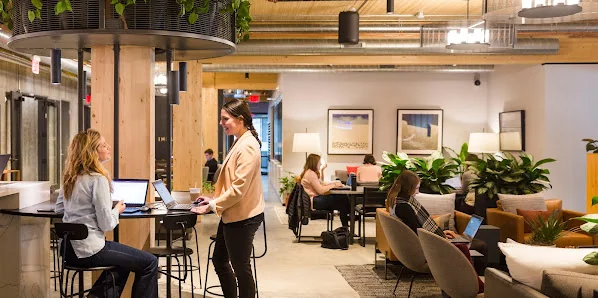 Industrious Orlando open coworking lounge with hanging greenery on wooden columns, plants, and warm lighting