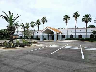 Gulf Breeze Cowork Annex single-story commercial building with peaked roof entrance, tall palm trees, and large parking lot
