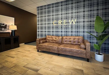 Crew CoWork welcoming lobby with tufted leather couch, blue plaid accent wall with CREW signage, and potted plant