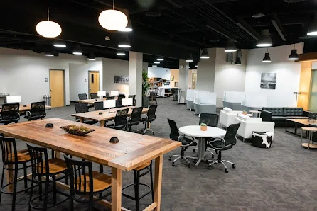 Work-Space at RDV large open coworking floor with dark ceiling, industrial pendant lights, wooden communal tables, and leather couch seating