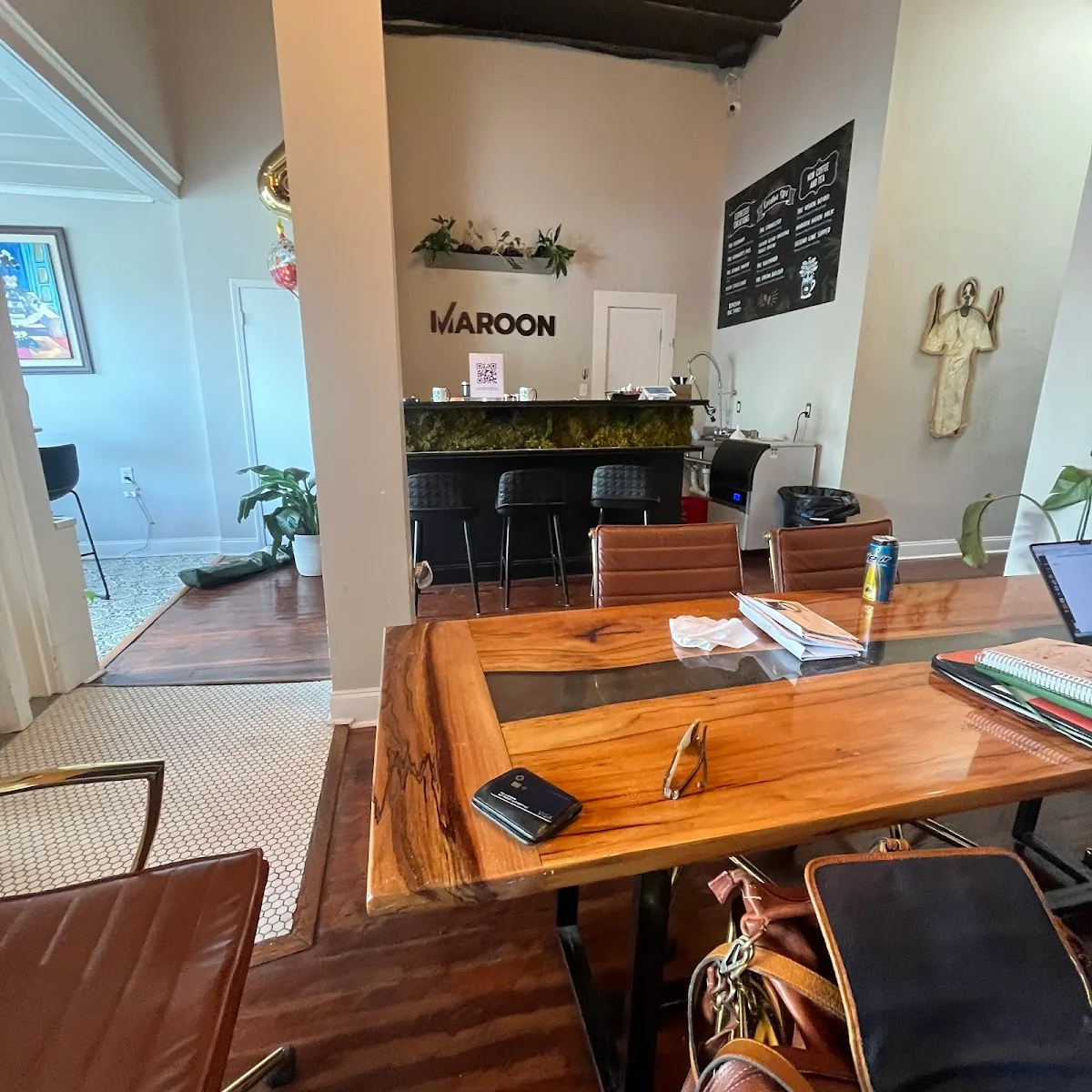 Maroon cafe-style coworking with live-edge wood table, brown leather chairs, moss-covered bar counter, MAROON wall signage, and eclectic decor